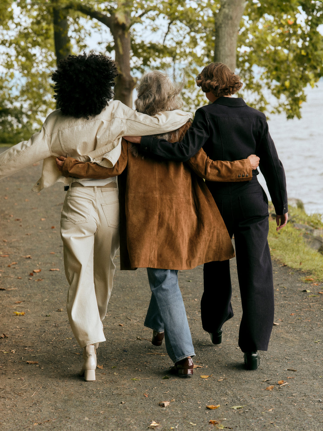 Three people walking together on a path by a body of water.